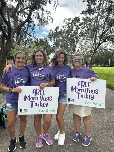 four ladies holding free mom hugs today signs